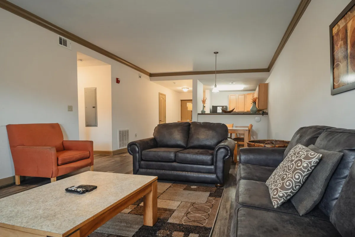 An open-plan interior view that seamlessly connects the living room with plush sofas and a coffee table to the adjacent dining area and kitchen. The layout emphasizes spaciousness and ease of movement, with ample natural light pouring in, creating a bright and welcoming environment ideal for both relaxing and socializing.