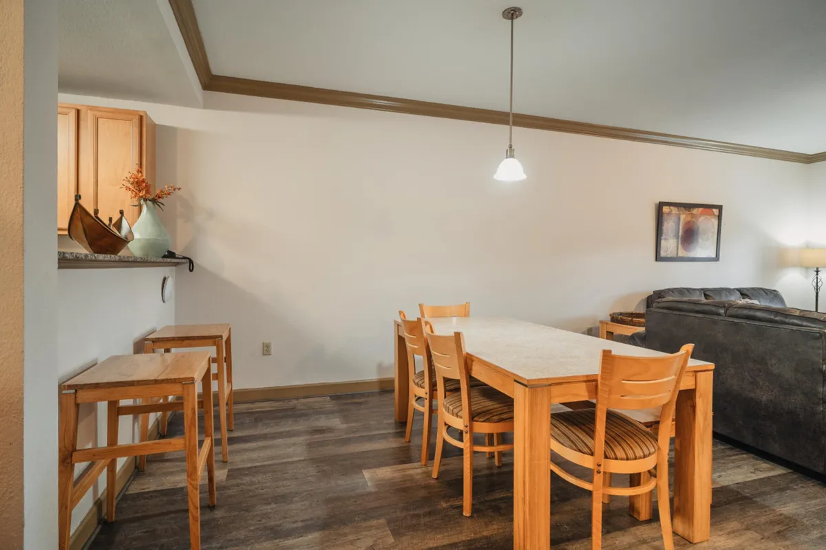 A warm, welcoming open area featuring a dining table, sofa, bar counter, and artwork—ideal for family dinners, casual gatherings, or game nights.