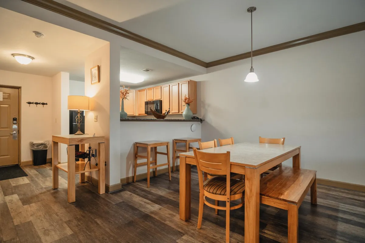 A dining area adjacent to the kitchen, featuring a dining table, bar stools, and an inviting kitchen area in the background. The layout encourages socializing and shared meals.