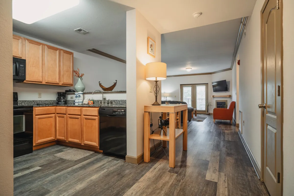 A view emphasizing the dining area with a well-set table, comfy seating, and a glimpse of the kitchen cabinets. Soft, natural light fills the space, inviting guests to gather for meals, games, or relaxed mornings. The arrangement is cozy yet functional, serving as a natural extension of the central living area.
