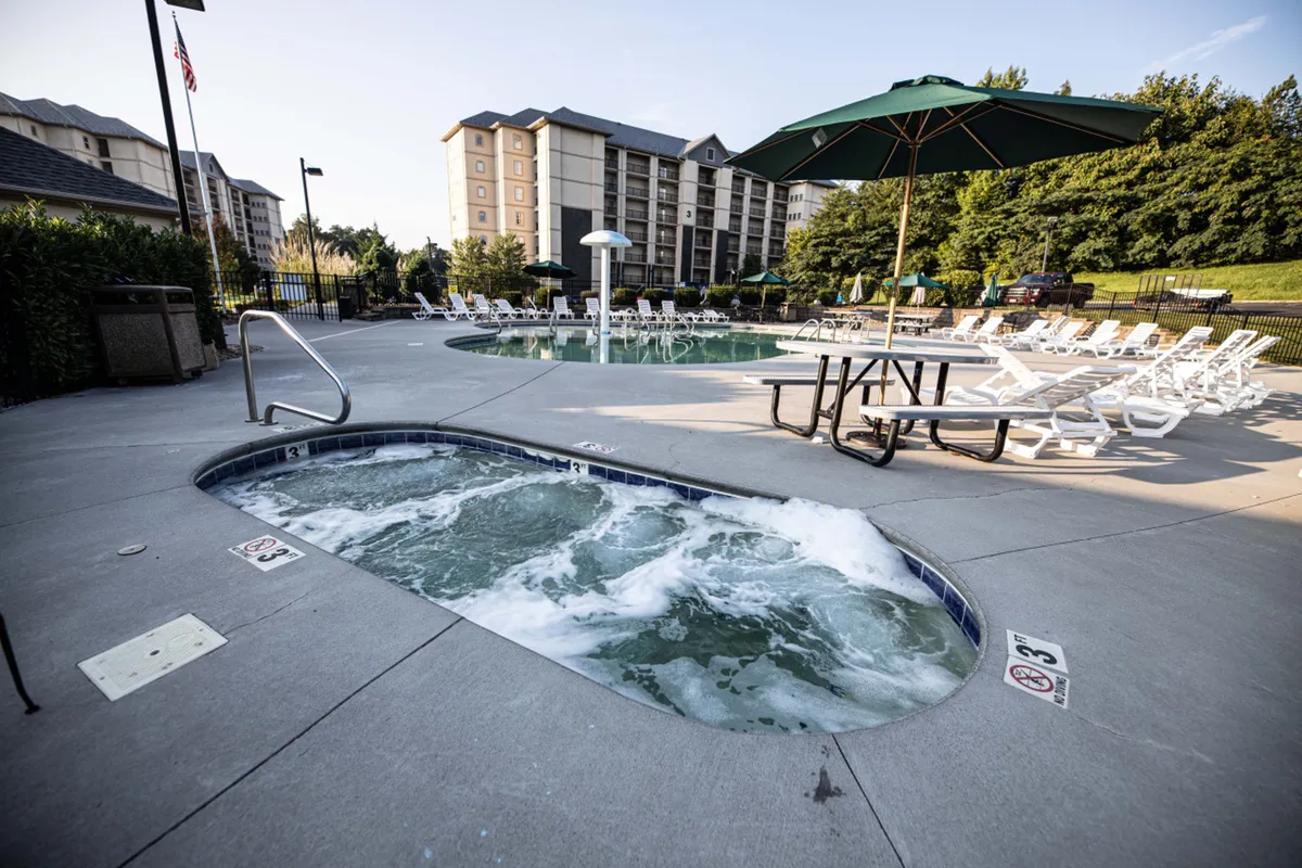 A vibrant outdoor area featuring a swimming pool, hot tub, lounge chairs, a picnic table, and an umbrella, all surrounded by greenery. The amenities encourage socializing, sunbathing, and outdoor meals, creating a lively and inviting atmosphere.