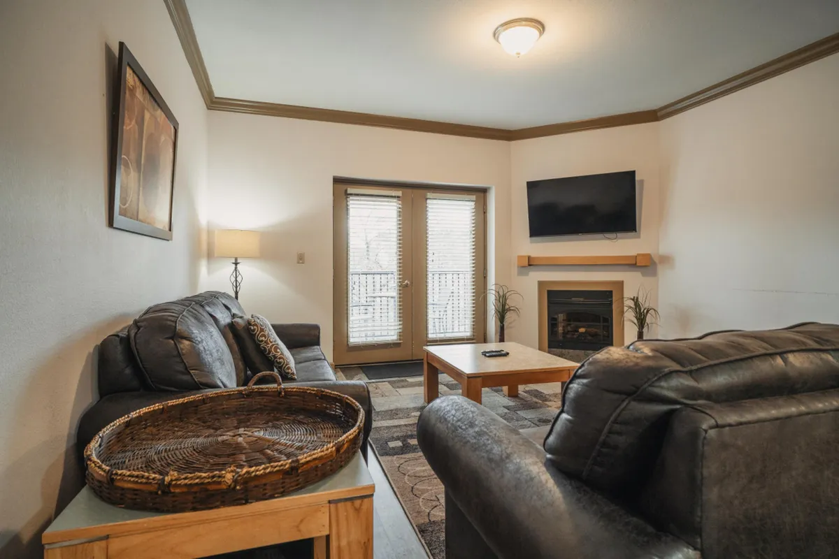 A cozy living space with a sofa, coffee table, television, fireplace, and sliding doors leading outdoors, blending interior comfort with a subtle connection to the outdoors.