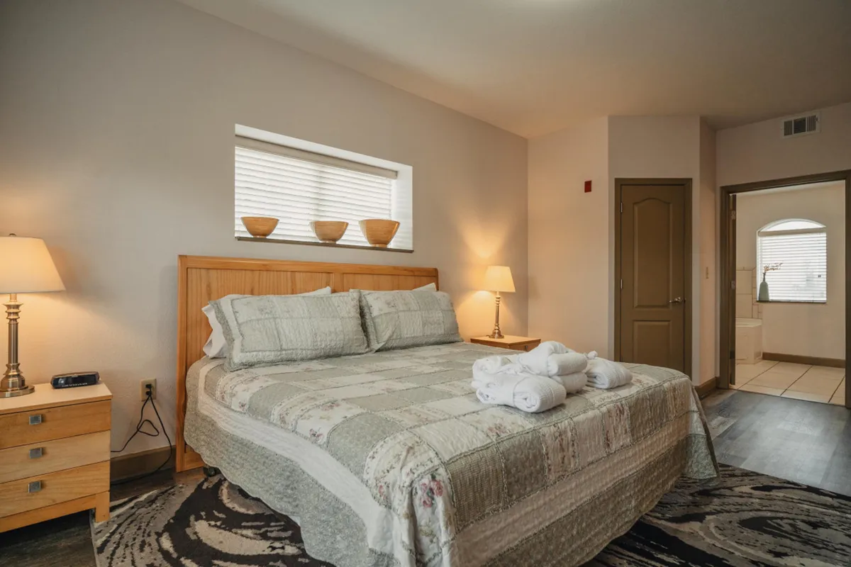 A tranquil bedroom with a cozy bed, nightstand, lamps, and a window. Bowls sit on the windowsill, adding a touch of charm. The room exudes relaxation and comfort, suitable for quiet mornings or peaceful nights.