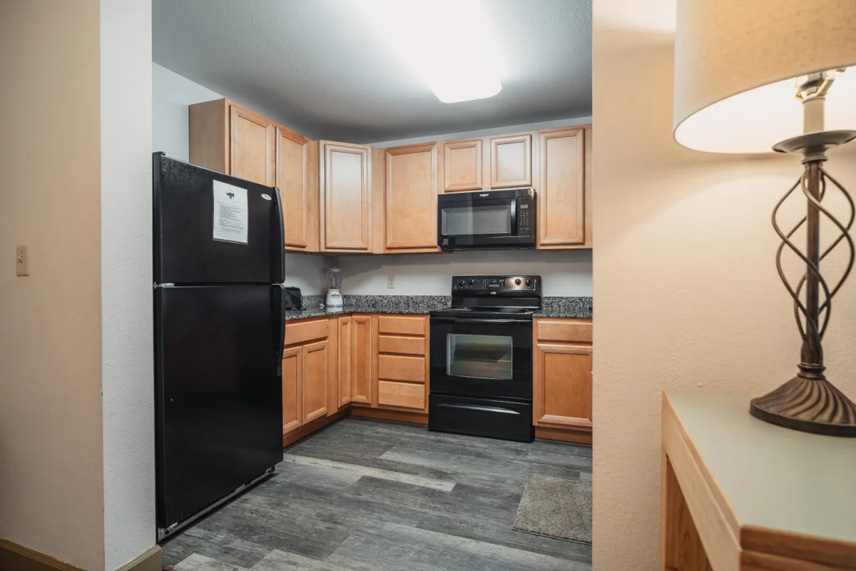 The kitchen is showcased from another angle, with a black refrigerator, stainless steel appliances, granite countertops, and wood cabinets. The scene feels set for family gatherings and meal prep.
