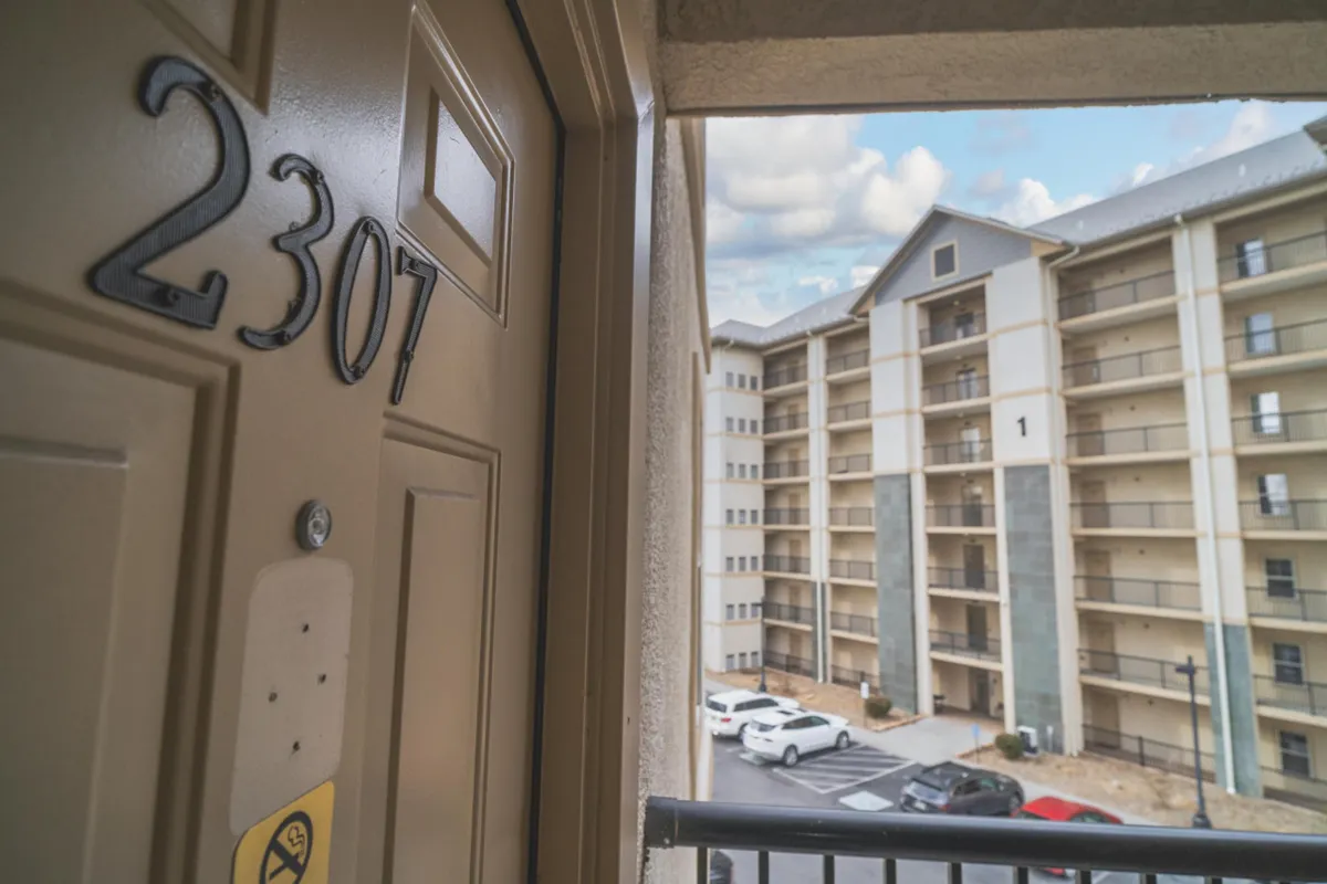 The photo captures the entrance to unit 2307, showing the door, a glimpse of the building's exterior, and the parking area. It highlights the transition from public to private space, emphasizing both accessibility and privacy.