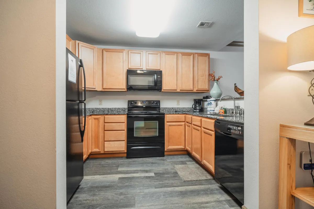A welcoming kitchen featuring black appliances, granite countertops, and warm wood cabinetry. The space is ready for cooking, with visible cookware and utensils making it feel both practical and inviting.